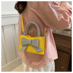 Détail d'un sac à main carré jaune vif orné d'un nœud étincelant en strass argentés