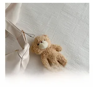 Close-up of a brown fluffy teddy bear charm with metallic chain on a white leather bag