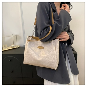 Detail of woven cream leather tote bag featuring a gold metal logo plate and brown strap