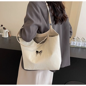 Close-up of a cream tote bag with a liquid metal butterfly badge and pleated texture