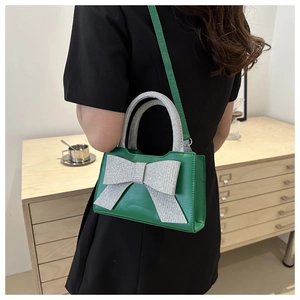 Détail d'un sac à main vert avec un grand nœud pailleté argenté et bandoulière fine