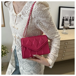 Detail of fuchsia quilted shoulder bag with woven chain strap held by a model
