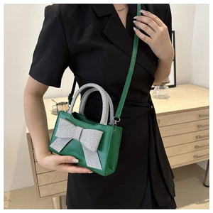 Détail d'un mini sac en cuir vert avec un nœud argenté scintillant et une bandoulière