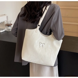 Detail of white textured leather tote bag with silver butterfly accent on grey blazer