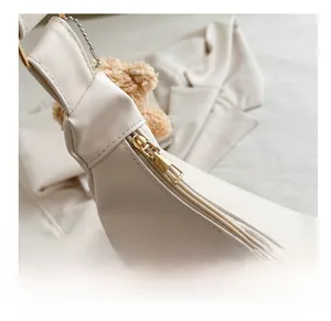 Detail of cream leather shoulder bag with gold zipper and brown plush bear charm