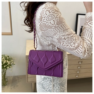 Detail of dark purple quilted leather shoulder bag with gold chain strap worn by a model