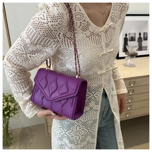 Detail of purple quilted crossbody bag with golden chain strap and wave pattern finish