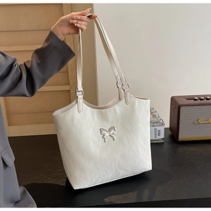 Detail of a large cream tote bag with elegant butterfly buckle and pleated texture