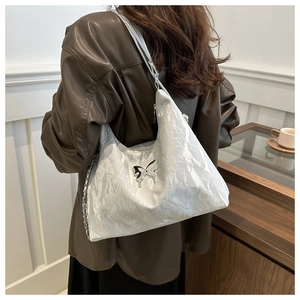 Detail of silver pleated shoulder bag with a metallic butterfly charm and texture