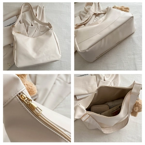 Detail view of cream shoulder bag with plush bear charm and golden zipper details