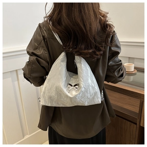 Silver wrinkled crossbody bag with butterfly pendant worn over a brown leather jacket