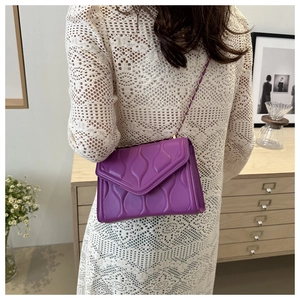 Detail of purple quilted chain crossbody bag styled with a white crochet dress