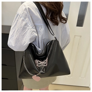 Detail of black glossy leather tote bag featuring pink butterfly and heart charms