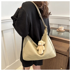 Detailed shot of a beige hobo bag with a cute plush bear charm on a female shoulder