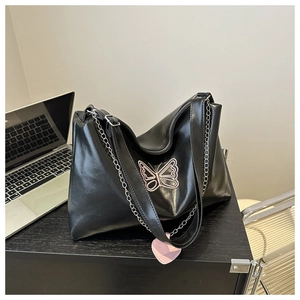 Detail of pink butterfly embroidery and heart pendant on a black leather tote bag
