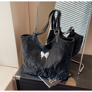 Detail of black pleated leather tote bag featuring a metallic silver butterfly ornament