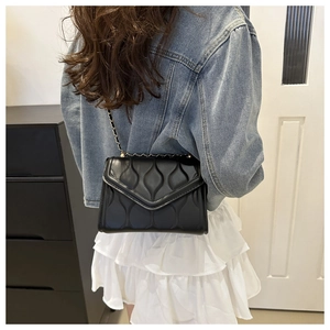 Detail of black quilted underarm bag with wavy stitching and slim metal chain strap