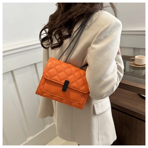 Detail of classic quilted orange crossbody bag with black buckle and metal chain strap