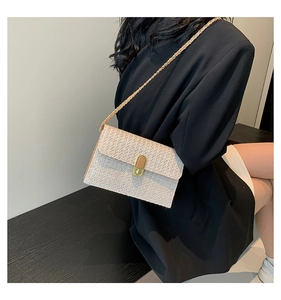 Close-up of straw crossbody bag featuring a golden twist lock and chain strap detail