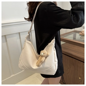 Detail of off-white hobo bag with wide strap and a cute brown plush bear charm accessory