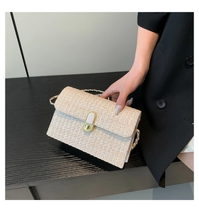 Close-up of cream woven crossbody bag with gold chain strap and metal clasp on wood