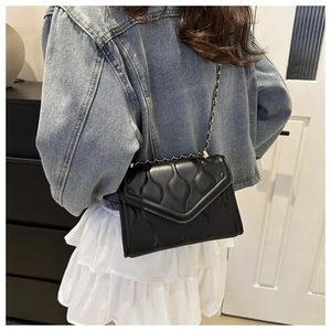 Quilted black chain crossbody bag featuring wave texture on a denim casual outfit