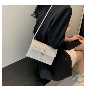 Detail of white woven straw crossbody bag with golden chain strap and oval twist lock