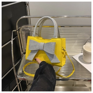Détail d'un sac à main jaune avec un grand nœud en strass et une poignée pailletée