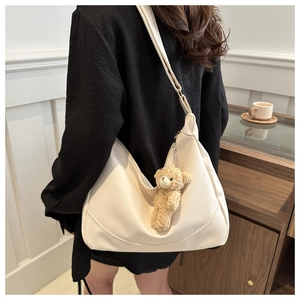 Detail of cream crescent shoulder bag with cute brown plush bear charm and adjustable strap