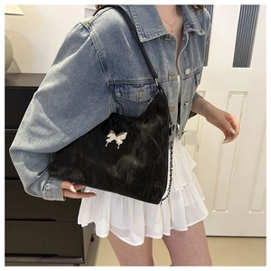 Detail of black crossbody bag featuring a silver metal butterfly ornament on velvet texture