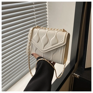 Detail of cream crossbody bag with wavy quilted texture and golden chain strap