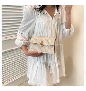 Detail of light beige straw woven crossbody bag featuring a gold metal lock and chain strap