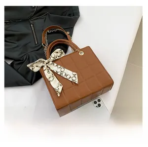 Brown quilted handbag with silk scarf detail and gold chain next to a phone for size comparison