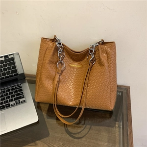 Brown woven textured large tote bag with silver chain strap on a desk with a laptop