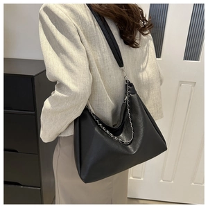 Detail view of large black leather shoulder bag with silver chain strap on model