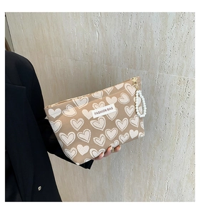 Detailed view of beige heart-print makeup bag with gold zipper and pearl handle