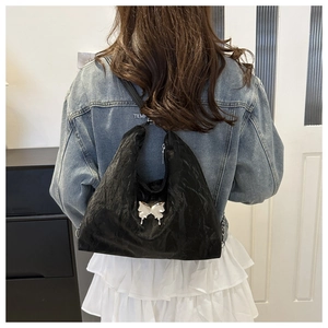 Detail of black pleated tote bag with silver butterfly charm shown on model shoulder