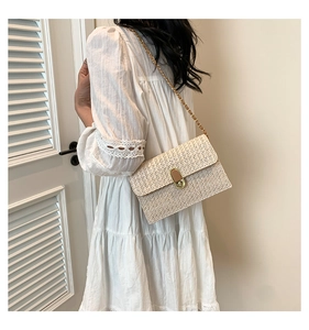 Detail of cream woven crossbody bag featuring a gold chain strap and metal lock closure