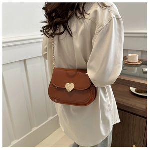 Brown patent leather shoulder bag with golden heart clasp shown on model in cafe