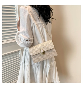 Detail of hand-woven straw crossbody bag with golden metal twist lock and chain strap
