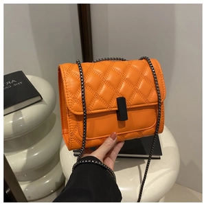 Détail d'un sac matelassé orange avec boucle noir mat et bandoulière en chaîne grise