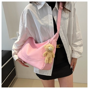 Pink crescent shoulder bag with plush bear charm worn by a model in a minimal setting