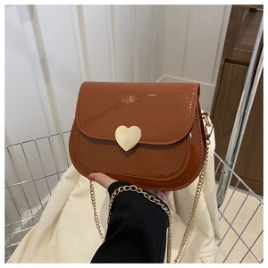 Detail of a brown patent leather square bag with a golden heart-shaped buckle and chain