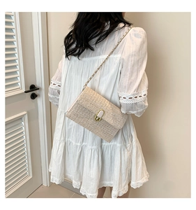 Detail of white straw crossbody bag with gold chain strap on a lace dress