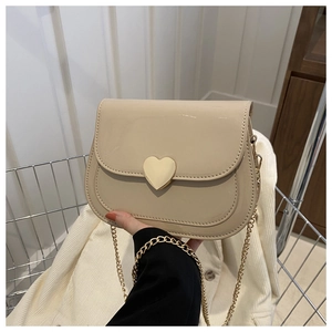 Close-up of a beige patent leather shoulder bag featuring a gold heart-shaped metal clasp