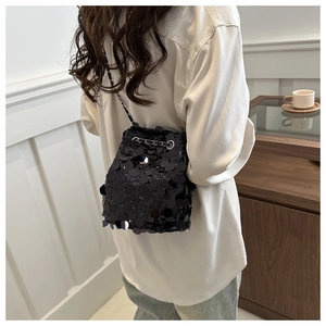 Close-up of black sequin bucket bag with metal chain strap worn by a model in soft light