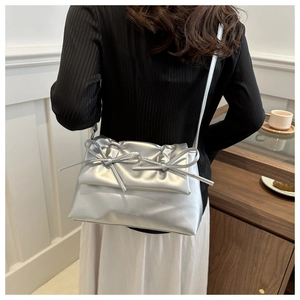Silver metallic crossbody bag with bows worn on shoulder in a lifestyle setting