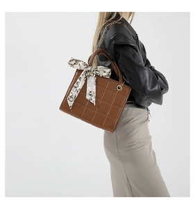 Brown quilted crossbody bag with silk scarf detail worn with a black leather jacket
