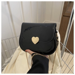 Detail of black patent leather crossbody bag with heart shaped metal lock and gold chain strap