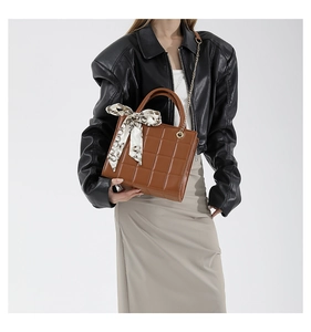 Detail of a brown quilted leather crossbody bag featuring a decorative silk scarf on the handle